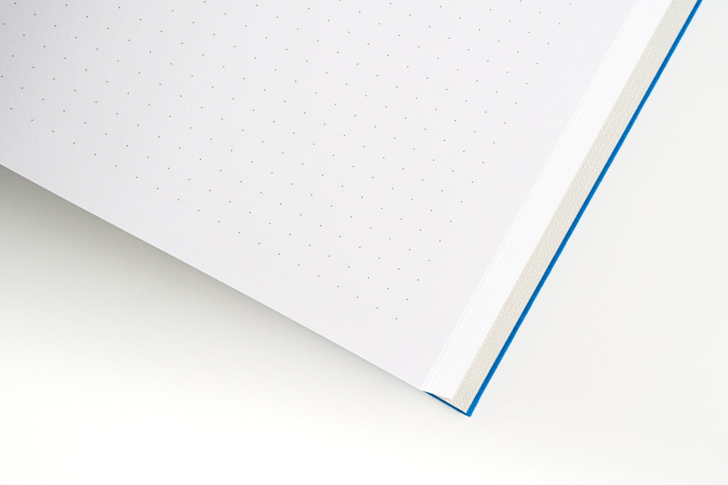 Nōto notebook lying open flat showing dot-grid pages and blue cover edge